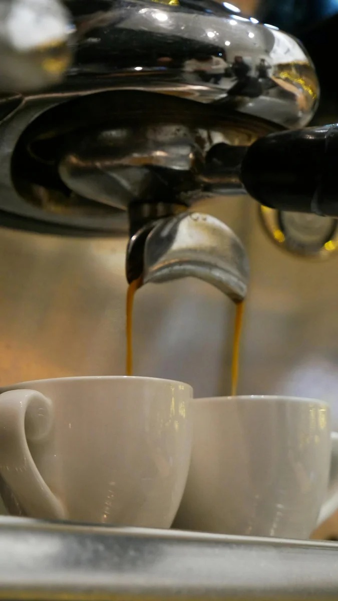 Espresso cayendo del portafiltros en dos tazas — extracción doble en cafetera profesional