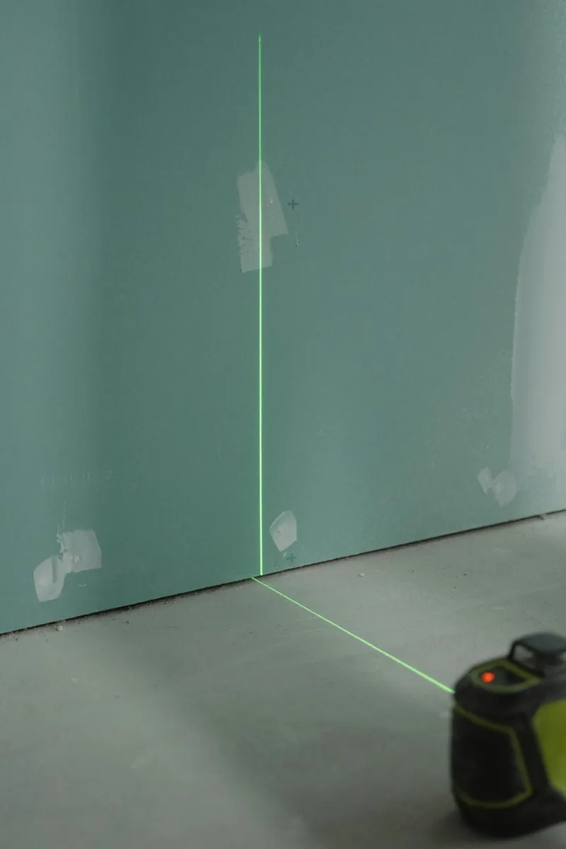 Líneas láser verdes proyectadas en pared durante instalación — nivel de líneas perfectamente alineado