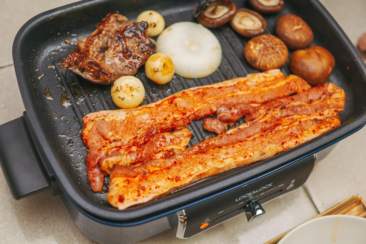 Tiras de cerdo y pollo cocinándose en plancha eléctrica con cebolla y champiñones