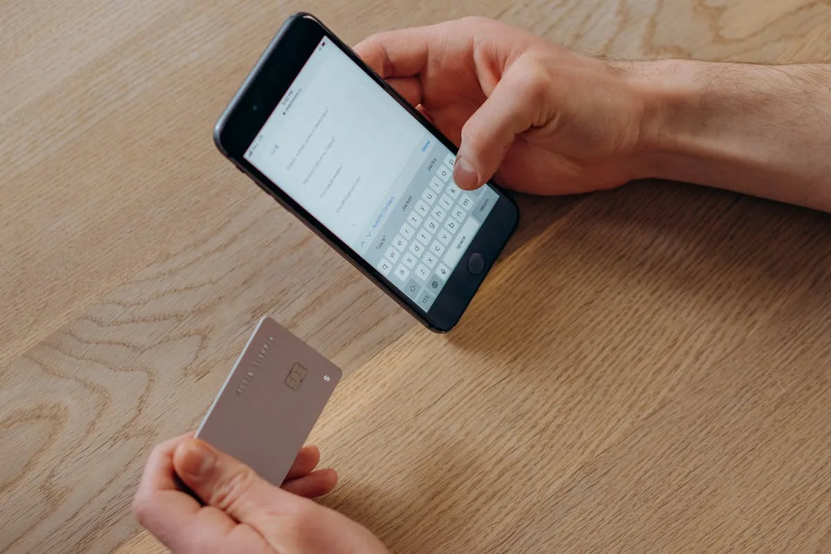 Mano sosteniendo tarjeta de débito junto a smartphone — gestión de pagos digitales