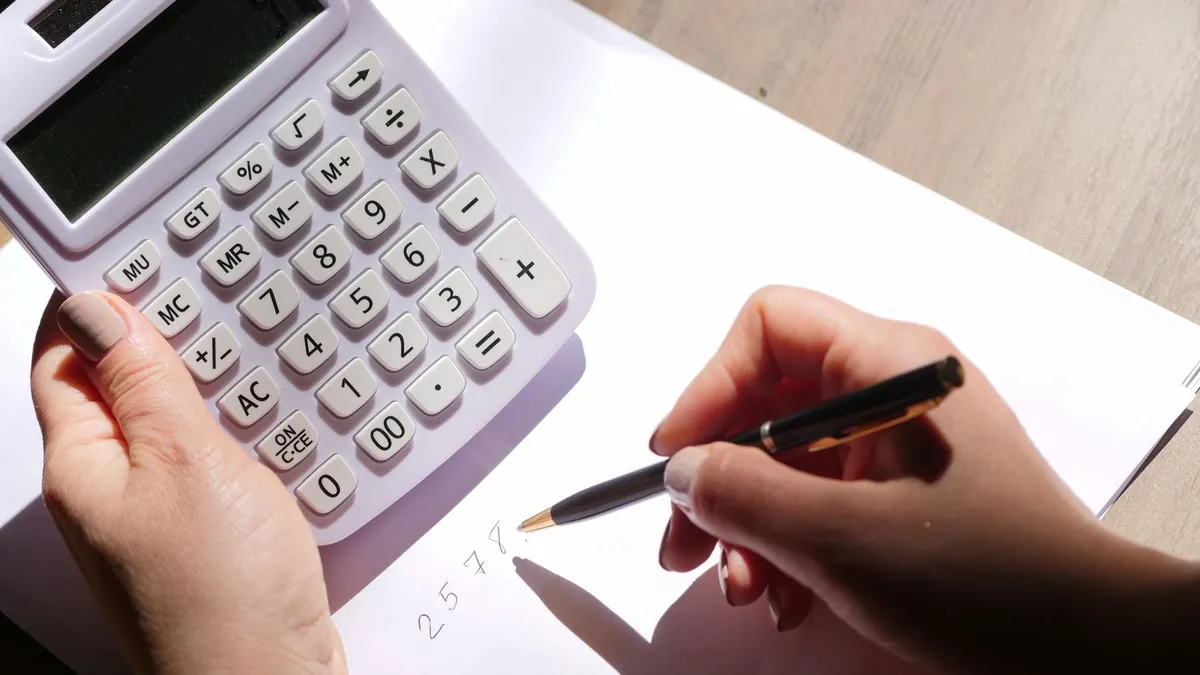 Mãos segurando uma calculadora e anotando contas em papel.