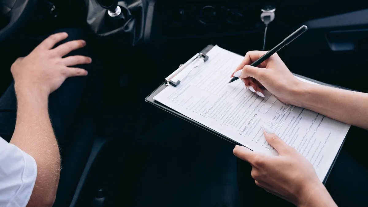Pessoa anota informações em uma prancheta no interior de um carro.