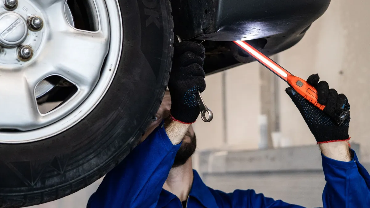Profissional ilumina a parte inferior de um carro elevado com uma lanterna de inspeção.