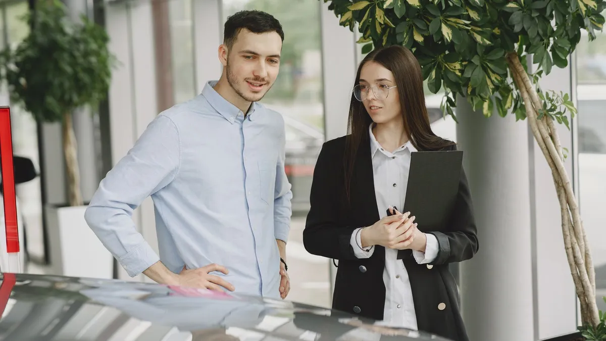 Duas pessoas conversam ao lado de um carro em um showroom.