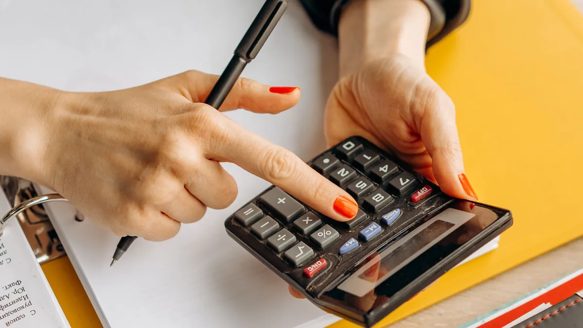 Mãos usando uma calculadora preta sobre papéis e uma pasta amarela.