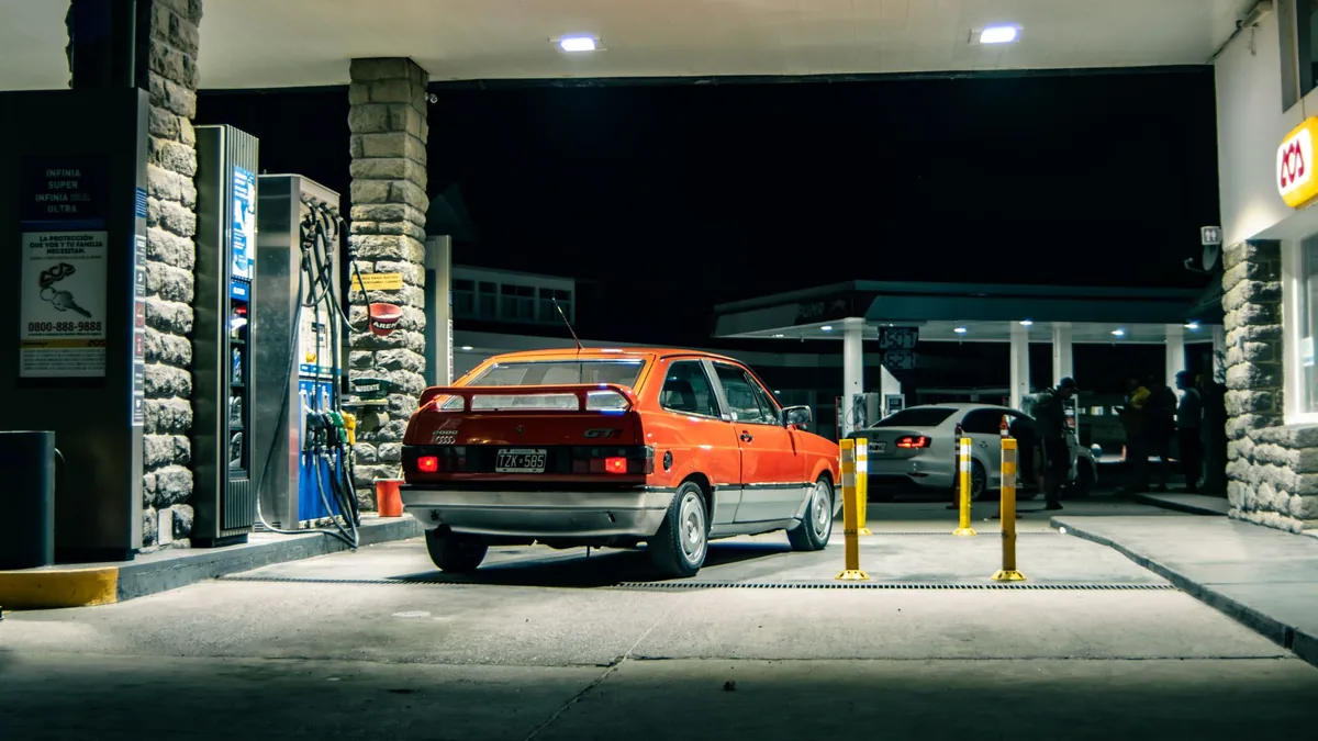 Vista traseira de um Volkswagen Gol vermelho em um posto à noite.