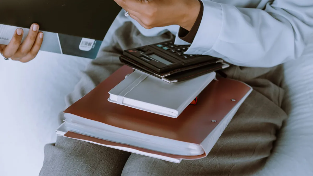 Pessoa segurando uma pasta aberta, com cadernos e uma calculadora no colo.