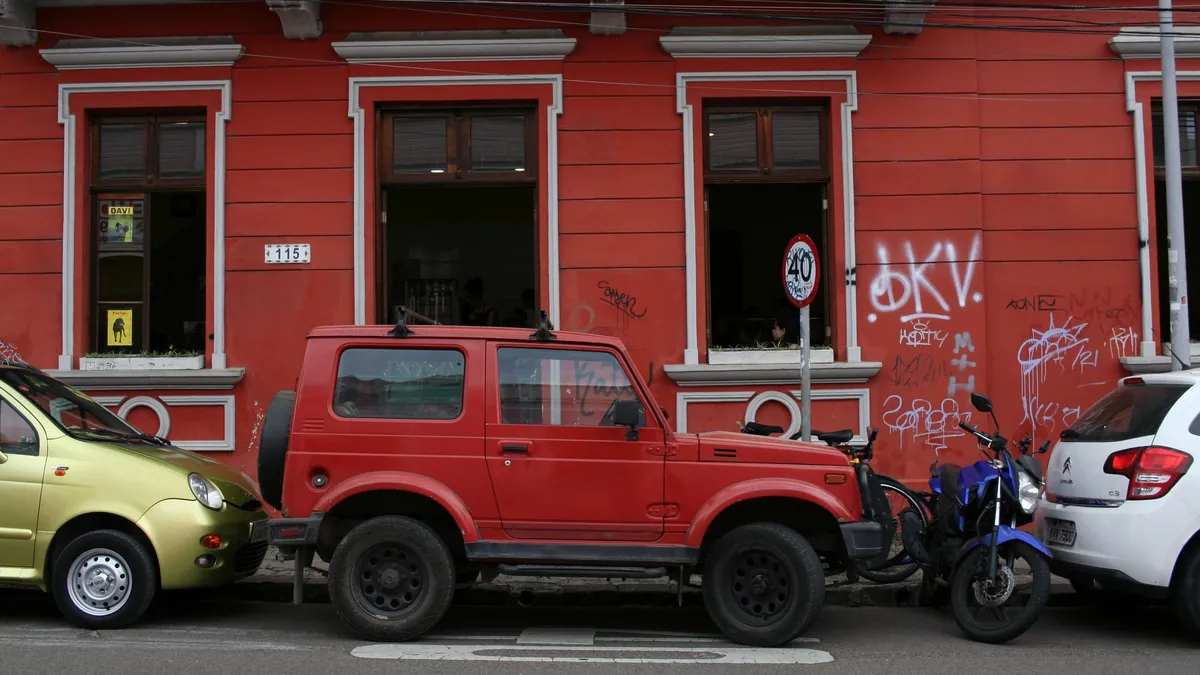 Carros e uma motocicleta estacionados diante de um prédio vermelho em Curitiba.